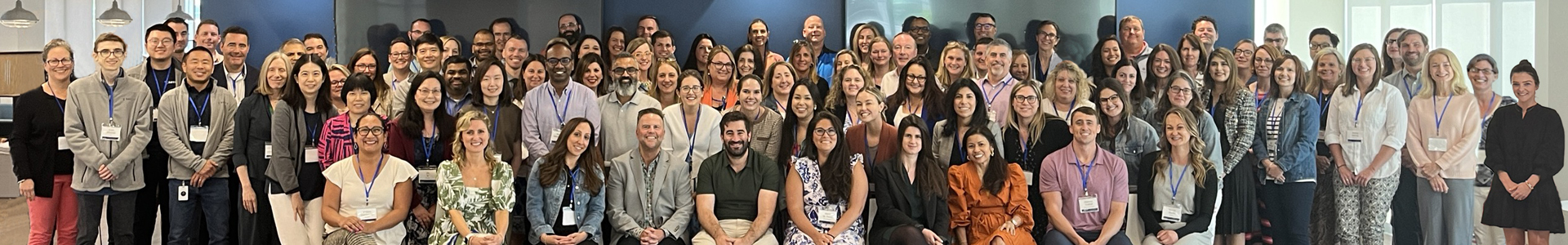 The full Amylyx team posing together in their cafeteria, arranged in five long rows.