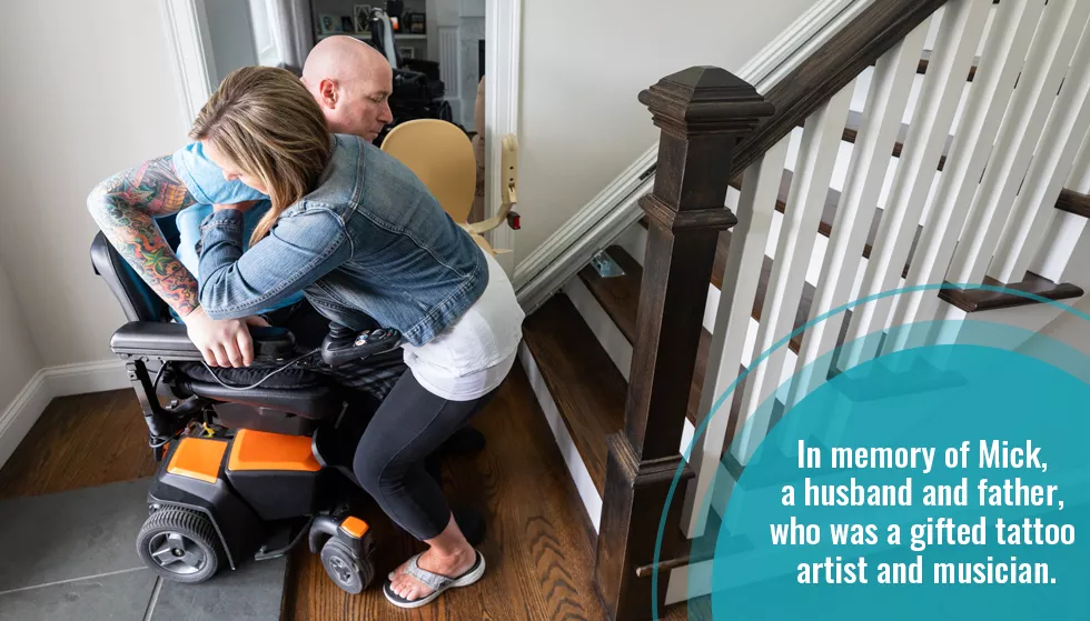 Person living with ALS being helped by caregiver out of electric wheelchair.