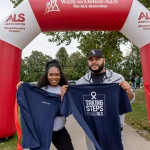 Amylyx employees holding up their company t-shirts at an ALS walk. The shirt reads "Taking steps to end ALS."