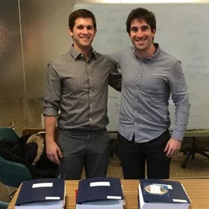 Co-founders Justin Klee and Josh Cohen in the early days of Amylyx, posing together behind a table of research.